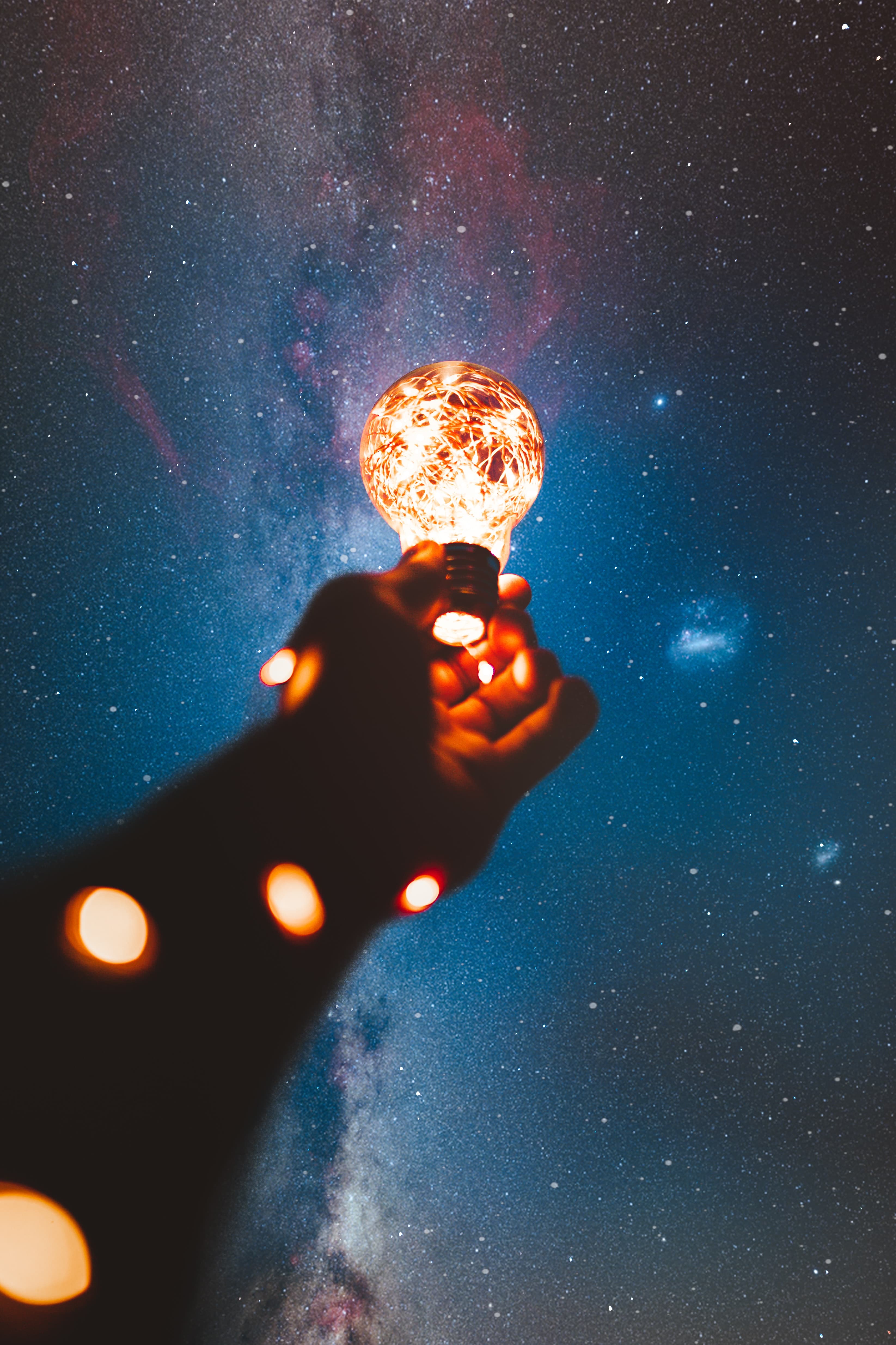 Hand holding a glowing light against a starry sky