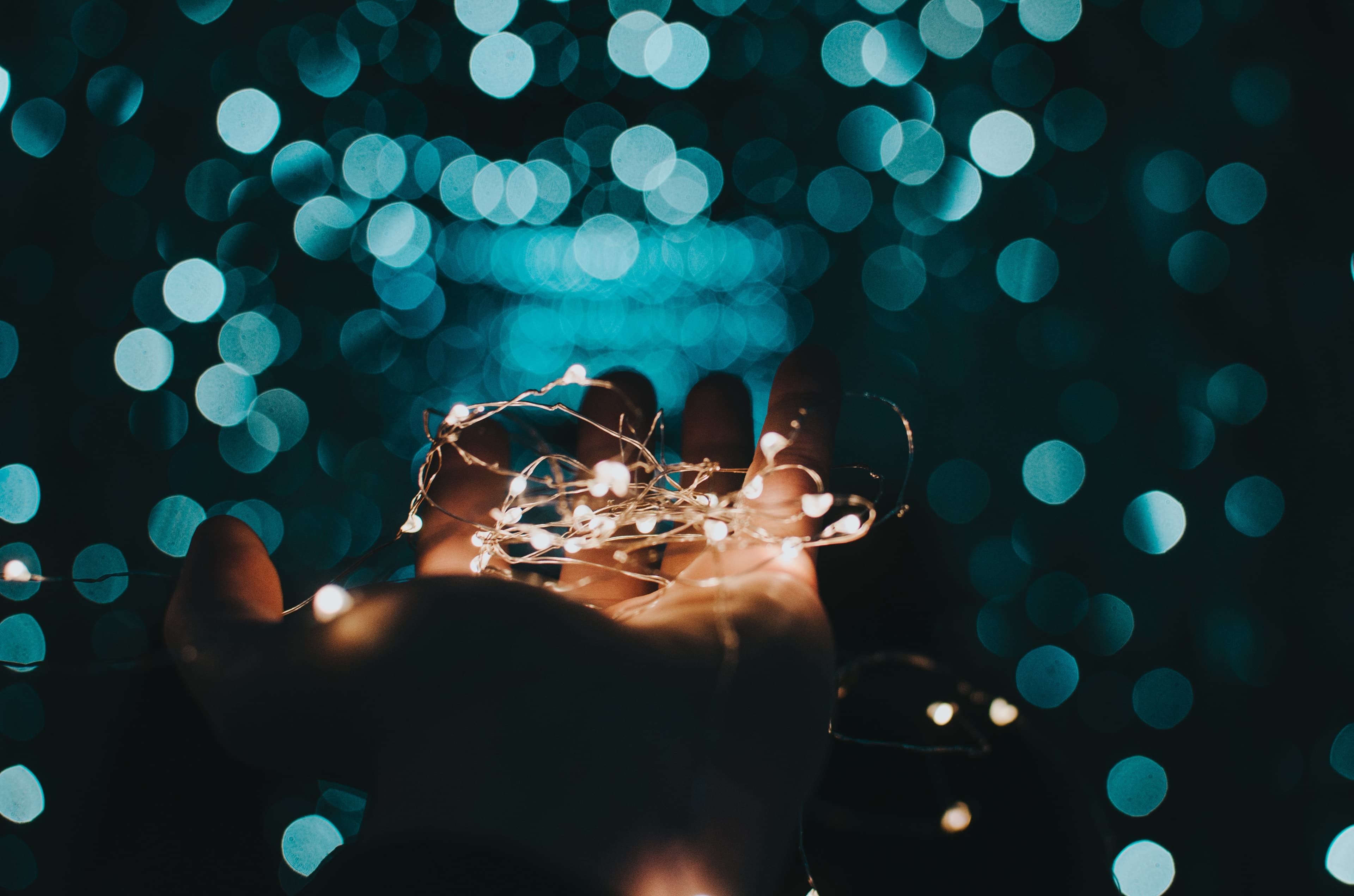 Hand holding string lights against teal bokeh
